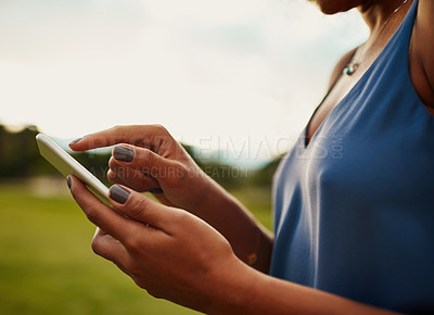 Buy stock photo Cropped shot of an unrecognizable woman using a smartphone while standing in a park during the day