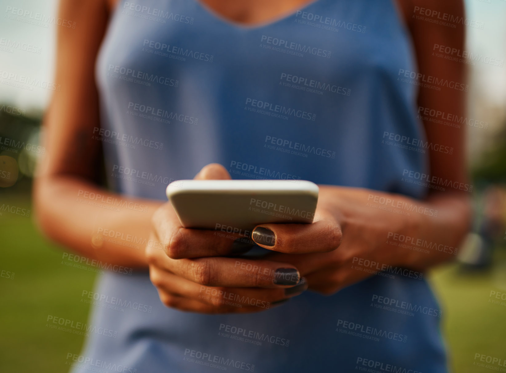 Buy stock photo Cropped shot of an unrecognizable woman using a smartphone while standing in a park during the day