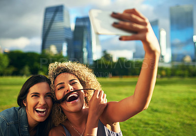 Buy stock photo Cropped shot of two attractive young girlfriends posing for a selfie together in a park