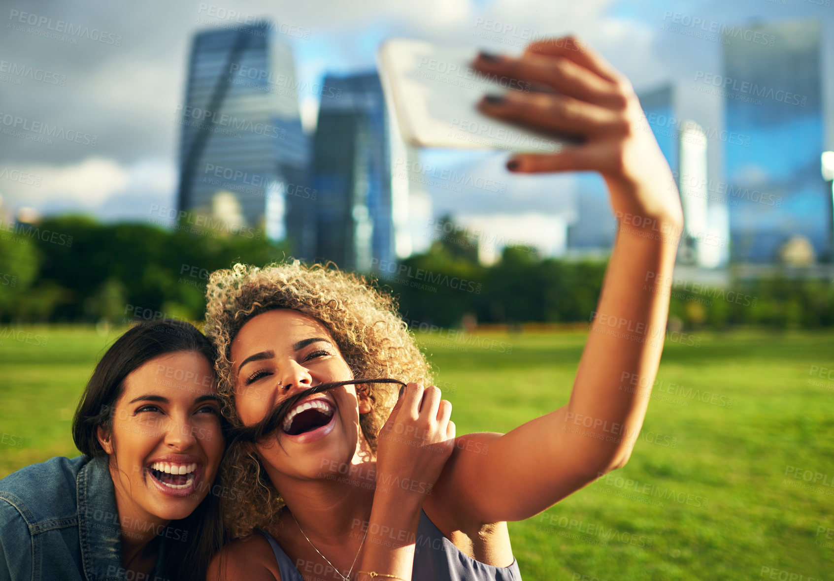 Buy stock photo Cropped shot of two attractive young girlfriends posing for a selfie together in a park