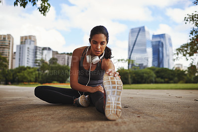 Buy stock photo Full length shot of an attractive young sportswoman doing stretch exercises outdoors in the city