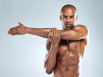 Buy stock photo Studio shot of an athletic young man doing stretching exercises while posing against a grey background