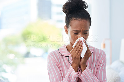 Buy stock photo Shot of a sickly young woman blowing her nose with a tissue at home
