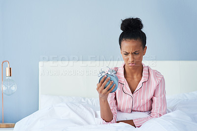 Buy stock photo Shot of an attractive young woman annoyingly looking at her alarm clock in bed at home