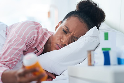 Buy stock photo Shot of an attractive young woman holding a bottle of pills in bed at home