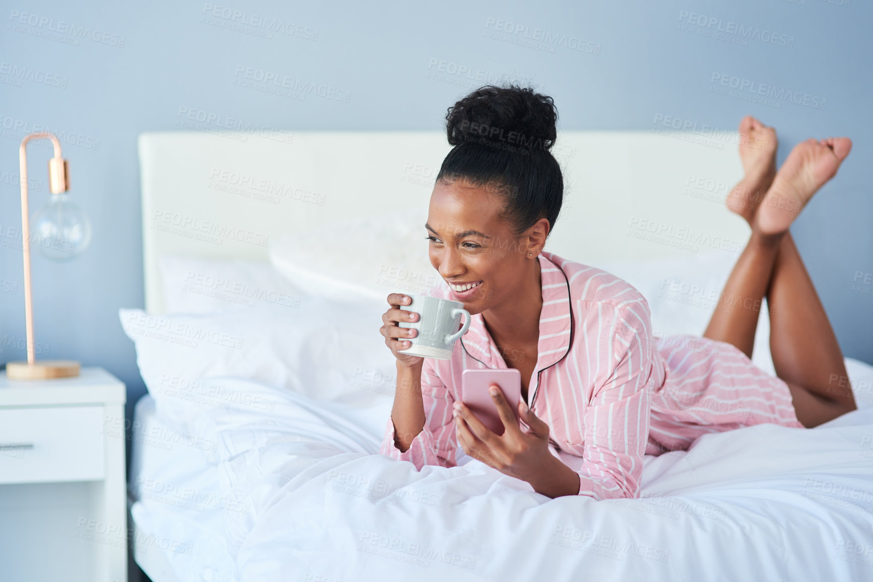 Buy stock photo Shot of an attractive young woman drinking coffee while using her cellphone in bed at home