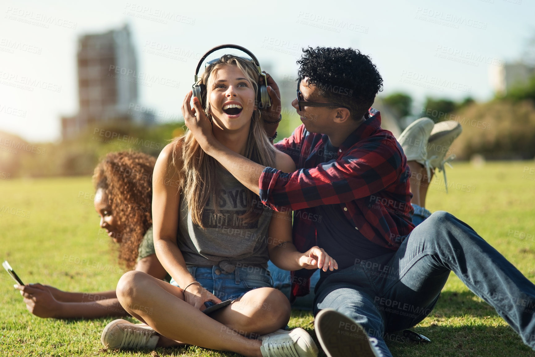 Buy stock photo Shot of a two cheerful young friends listening to music on headphones outside on a park during the day