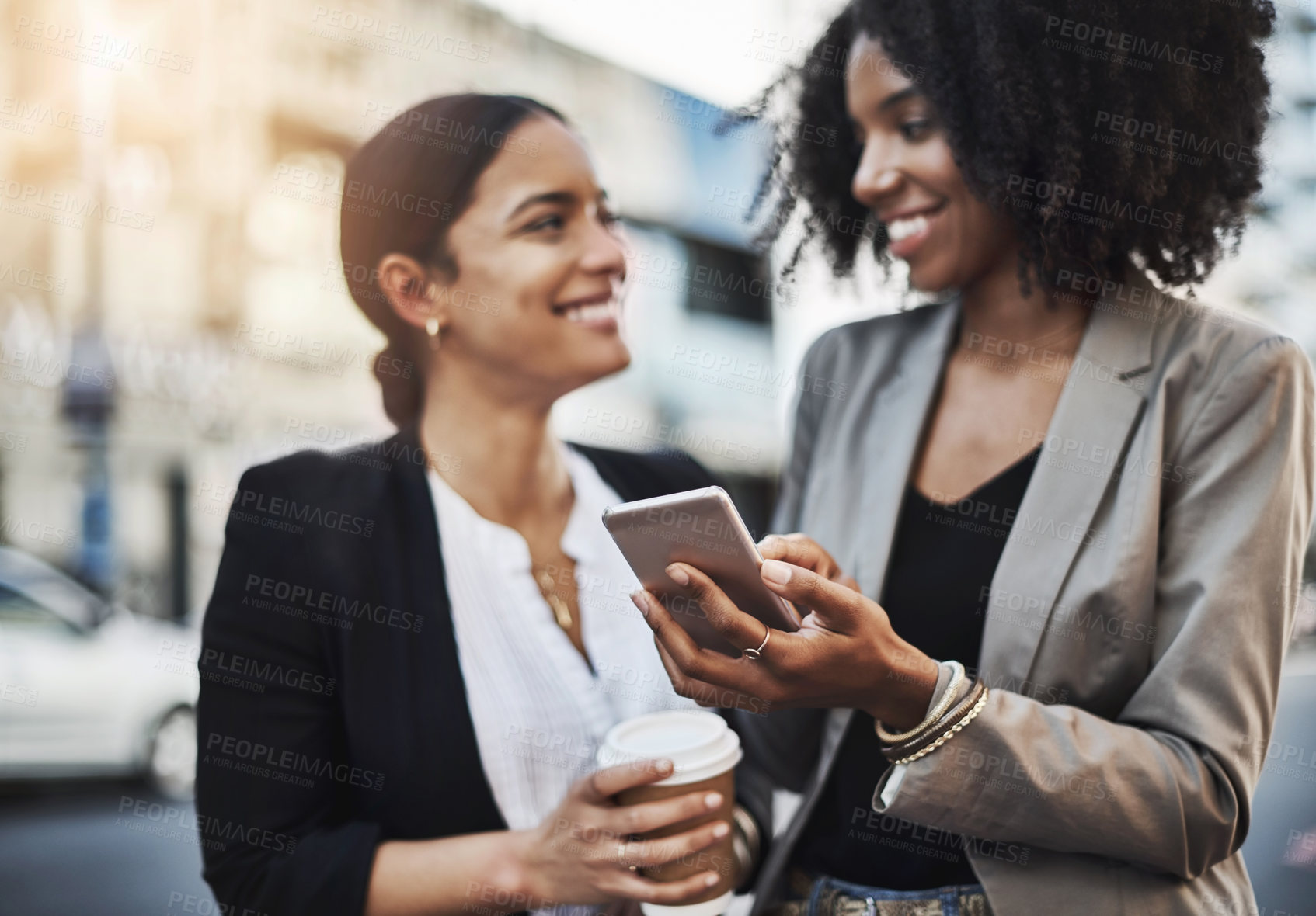 Buy stock photo Shot of two businesswomen looking at something on a cellphone in the city