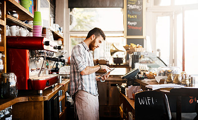 Buy stock photo Shot of a young man using a digital tablet while working in a coffee shop
