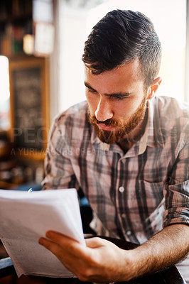 Buy stock photo Man, coffee shop and serious with paperwork for review as writer or author for editing or feedback. Male person, reading and writing on documents in restaurant as professional for media publication