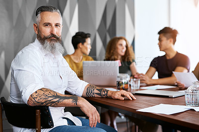 Buy stock photo Portrait of a mature businessman sitting in an office with his colleagues in the background