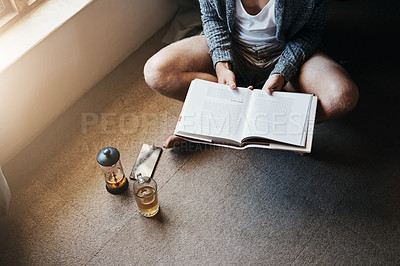 Buy stock photo High angle shot of an unrecognizable man reading a book while sitting on the floor at home