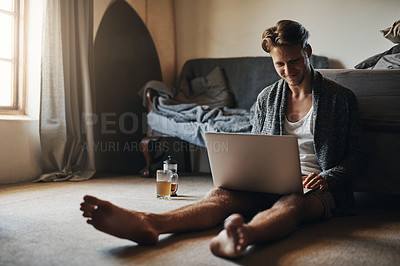 Buy stock photo Shot of a handsome young man using his laptop while sitting on the floor at home