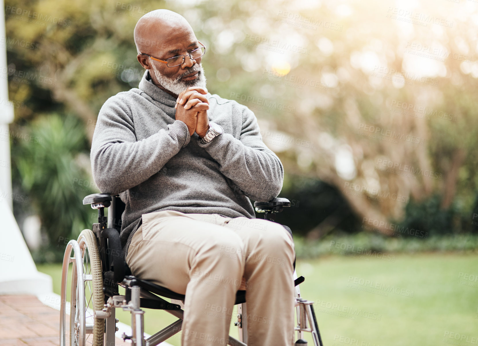 Buy stock photo Shot of a senior man holding his hands together while sitting in his wheelchair outside