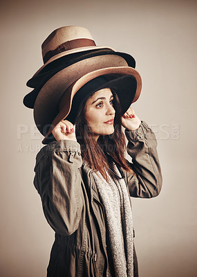 Buy stock photo Studio shot of a young woman wearing a pile of hats against a brown background