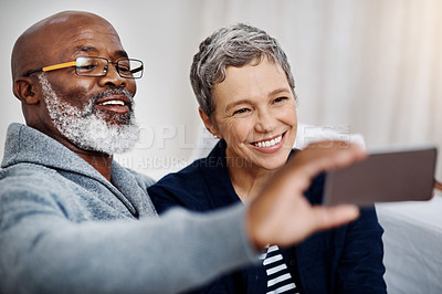 Buy stock photo Shot of an affectionate senior couple taking selfies while relaxing on the sofa at home