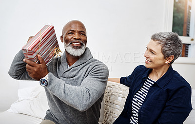 Buy stock photo Shot of an attractive senior woman surprising her husband with a gift at home