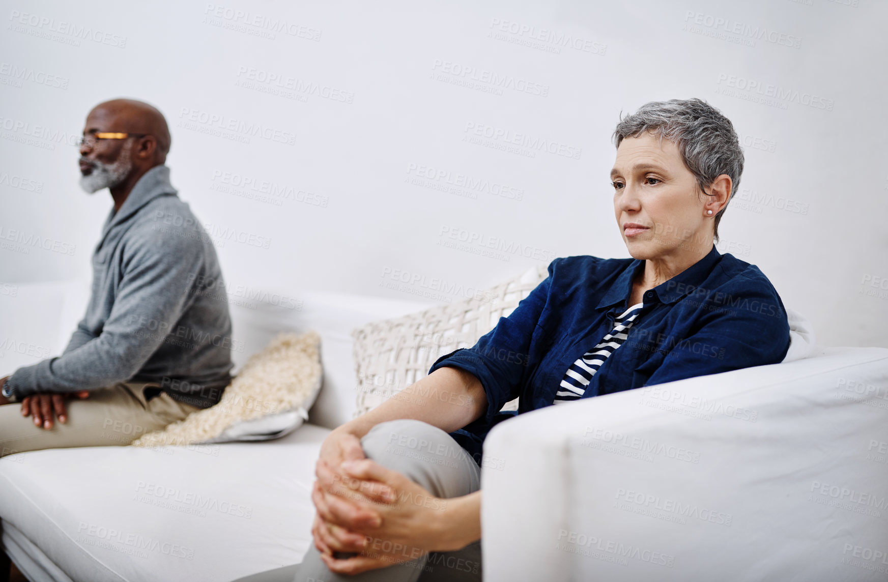 Buy stock photo Shot of an unhappy senior couple sitting separately on a couch after having an argument at home