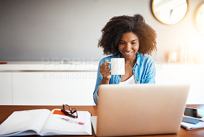 Buy stock photo Shot of an attractive young woman having a cup of coffee while working on her laptop at home