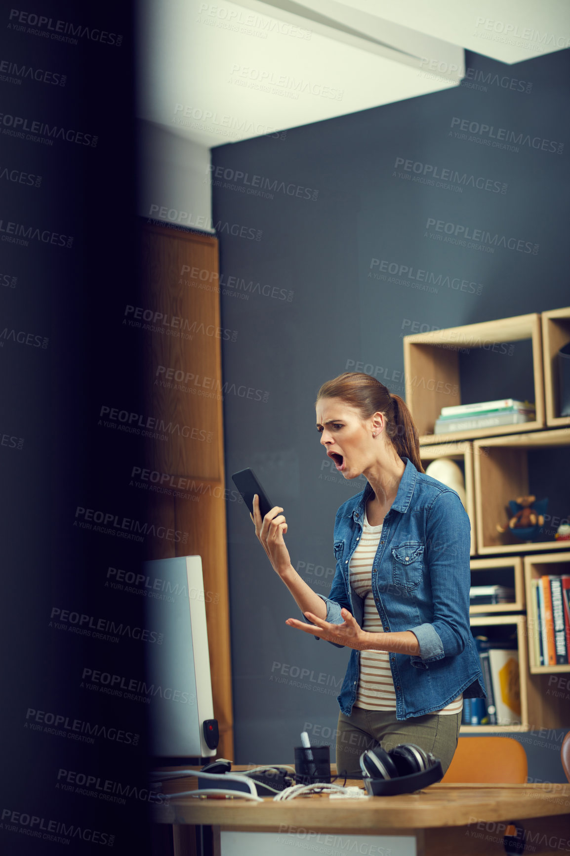 Buy stock photo Shot of a young businesswoman using a mobile phone and looking angry in a modern office