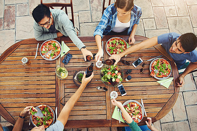 Buy stock photo High angle shot of a group young friends holding drinks and toasting together outside around a table