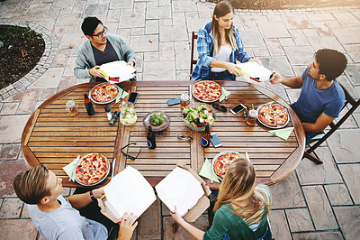 Buy stock photo High angle shot of a group of friends sitting around a table and enjoying pizza together outdoors