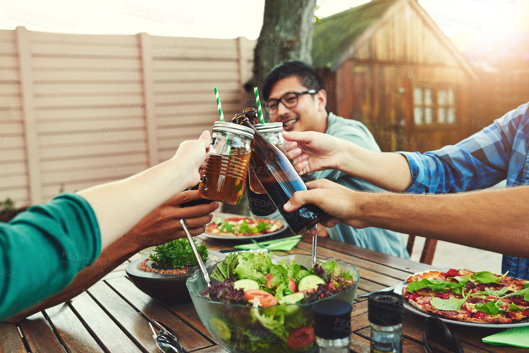 Buy stock photo Shot of a group of young friends holding up drinks and toasting to celebrate their friendship around a table outdoors