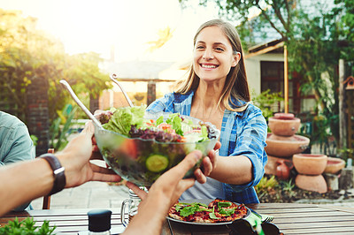 Buy stock photo Shot of young woman taking a salad bowl from a friend while sitting around a table outdoors