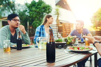 Buy stock photo Shot of a beer bottle on a table with a group of people enjoying themselves in the background
