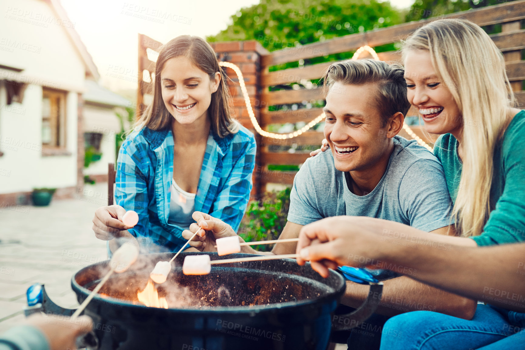 Buy stock photo Shot of a group cheerful young friends holding up marshmallows on sticks over a fire outside