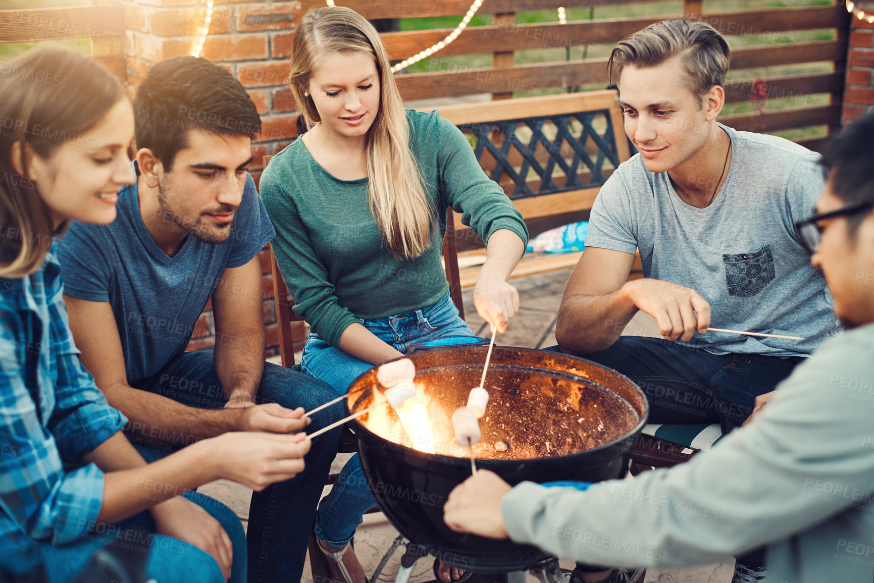 Buy stock photo Shot of a group cheerful young friends holding up marshmallows on sticks over a fire outside