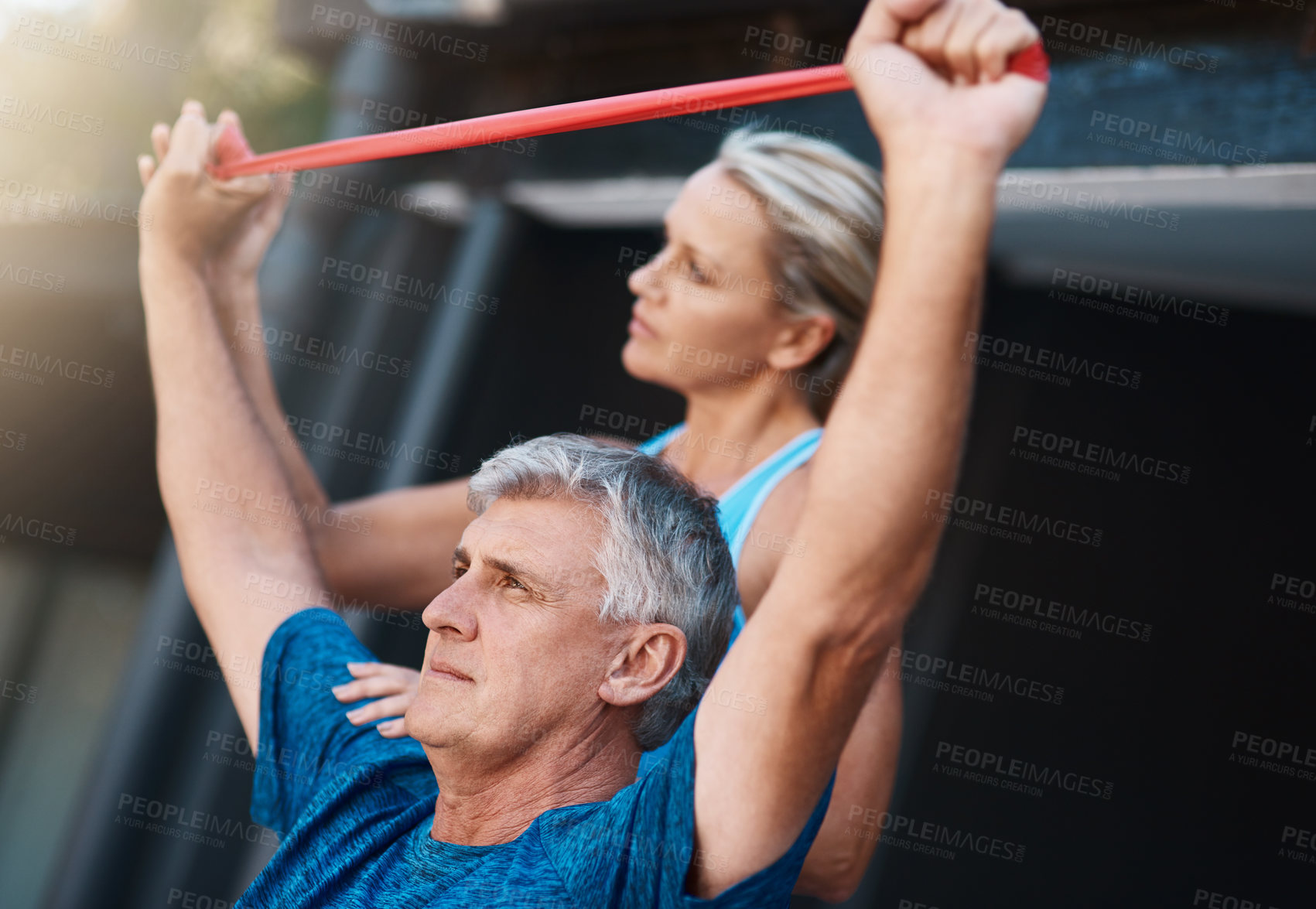 Buy stock photo Shot of a mature man stretching his arm muscles with an elastic band while being assisted by his wife