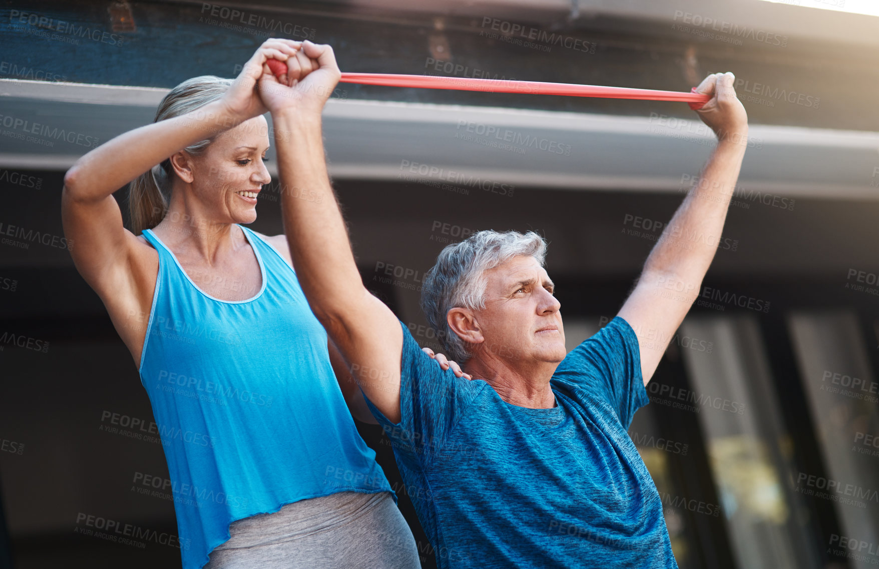 Buy stock photo Shot of a mature man stretching his arm muscles with an elastic band while being assisted by his wife
