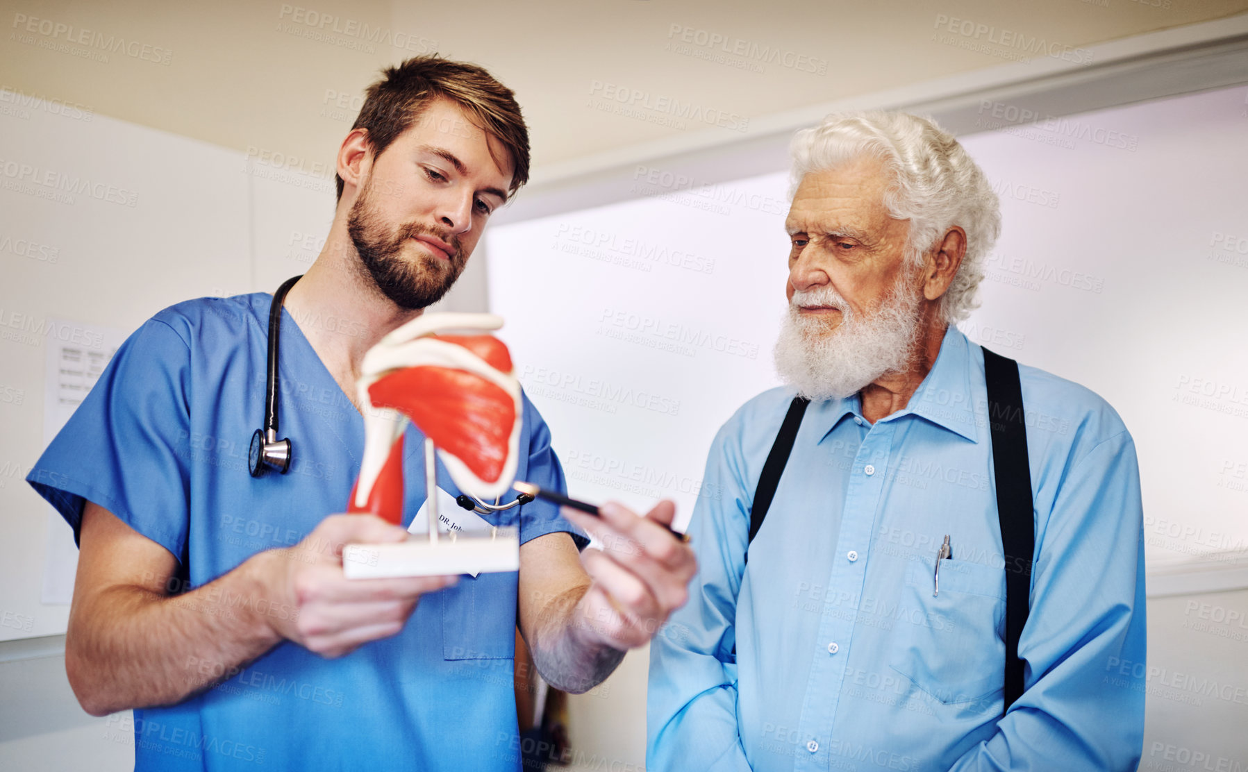 Buy stock photo Shot of a young doctor using a model to explain a diagnosis to his senior patient