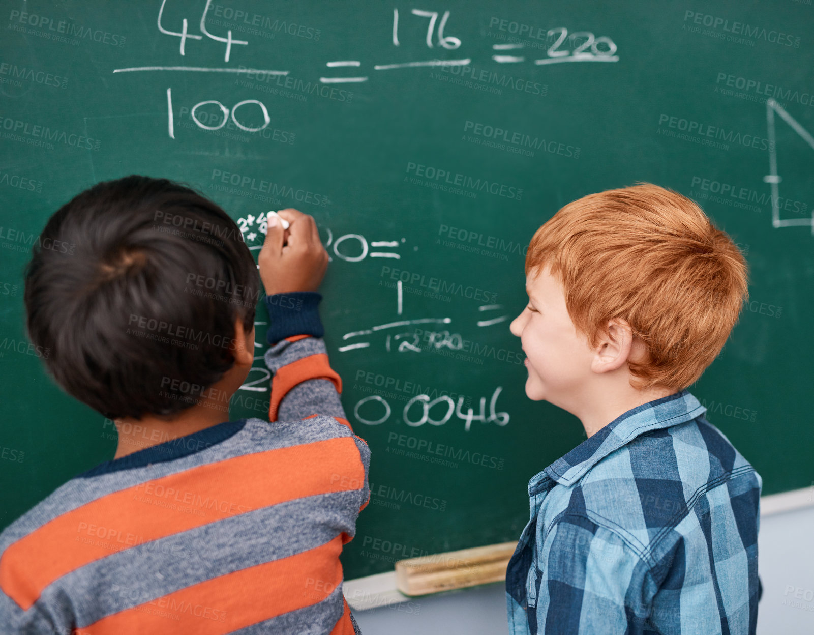 Buy stock photo Cropped shot of two focussed young elementary school kids writing answers to math questions on a green chalkboard in the classroom
