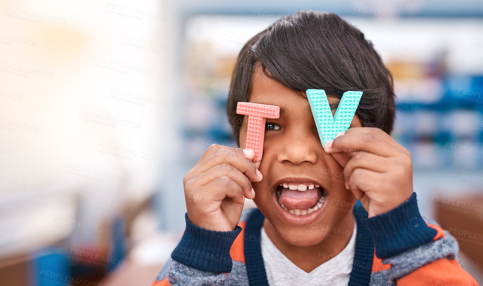Buy stock photo Cropped shot of a cheerful elementary school kid holding the letters T and V in front of his eyes inside of the classroom