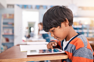 Buy stock photo Cropped shot of a focussed young elementary school kid browsing on a digital tablet inside of the class during the day