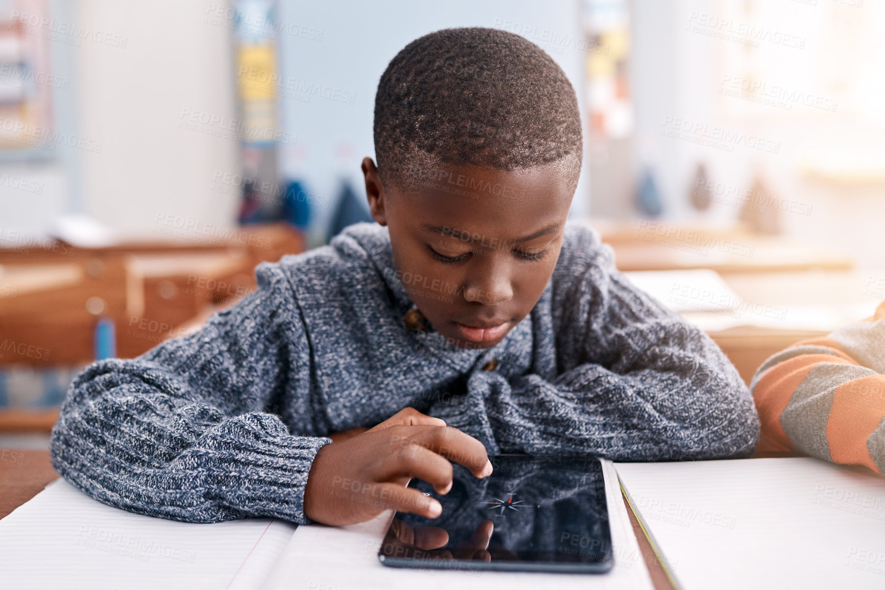 Buy stock photo Cropped shot of a focussed young elementary school kid browsing on a digital tablet inside of the class during the day