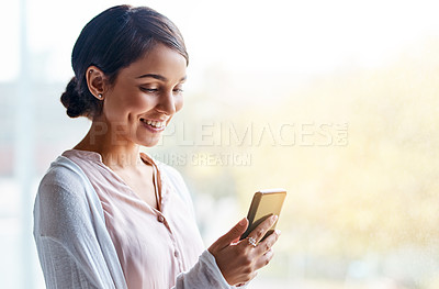 Buy stock photo Shot of a cheerful young female teacher standing inside of her classroom while texting on her cellphone during the day