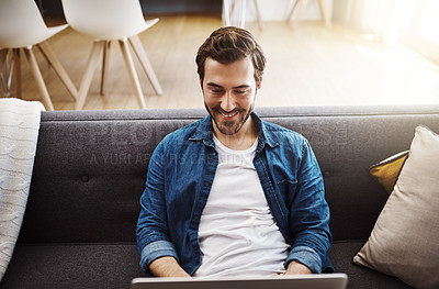 Buy stock photo Shot of a handsome young man using his laptop while relaxing on a sofa at home