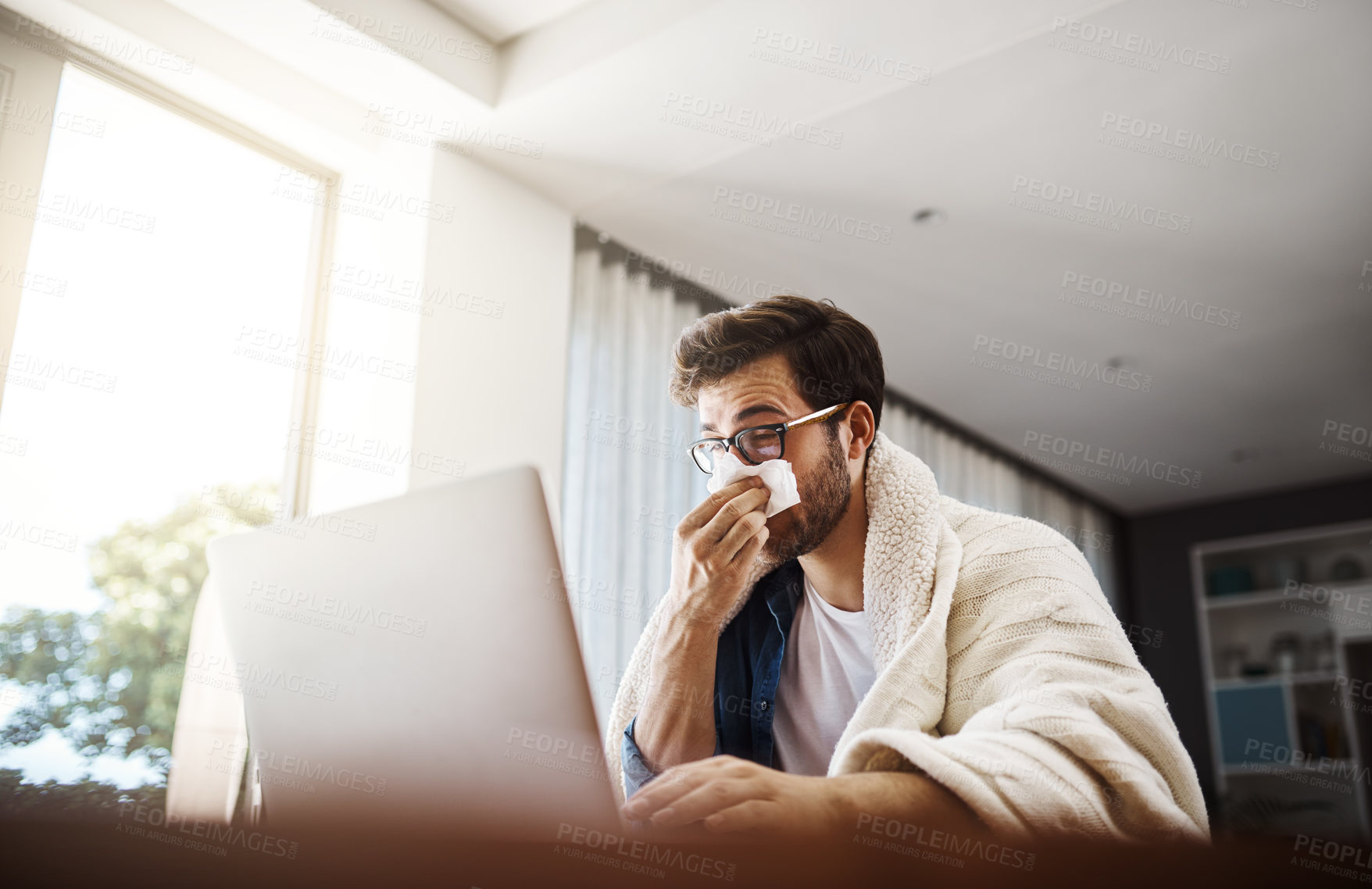 Buy stock photo Shot of a sickly young businessman blowing his nose with a tissue while working from home