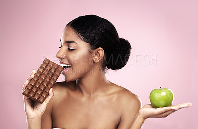Buy stock photo Studio shot of a beautiful young woman deciding between healthy and unhealthy snacks