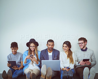 Buy stock photo Studio shot of a group of young businesspeople using wireless technology while sitting in line against a grey background