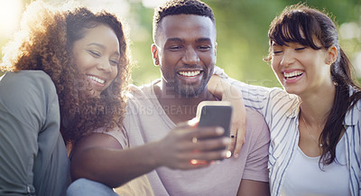 Buy stock photo Shot of a cheerful group of friends using a cellphone together while relaxing outdoors