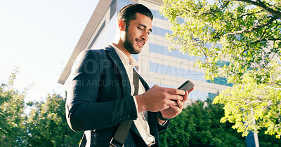 Buy stock photo Shot of a handsome young businessman using his cellphone while walking though the city