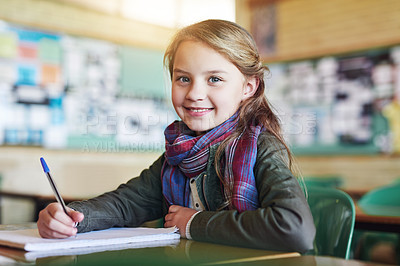 Buy stock photo Education, portrait of young girl in classroom and writing in her notebook at her desk in school building. Studying or homework, learn or academic and happy female student with pen sitting on chair