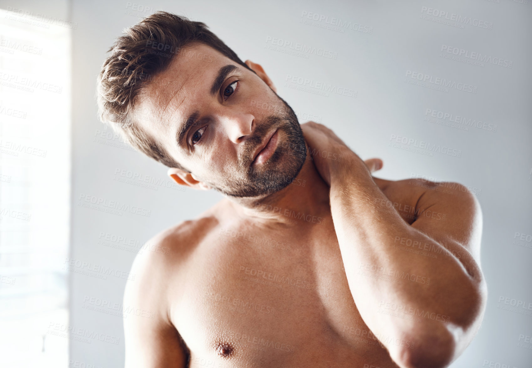 Buy stock photo Portrait of a handsome young man holding his neck in pain while relaxing at home