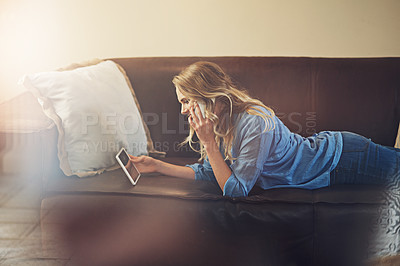 Buy stock photo Shot of a relaxed young woman using a digital tablet and smartphone on the sofa at home