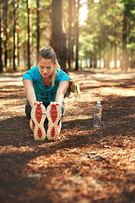 Buy stock photo Shot of a sporty young woman doing stretch exercise while out in nature