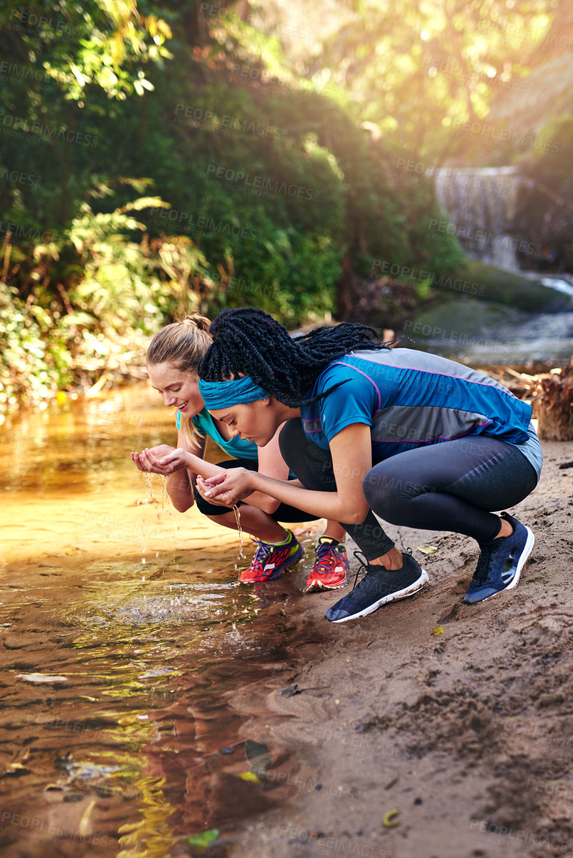 Buy stock photo Shot of two sporty young women drinking water from a water stream